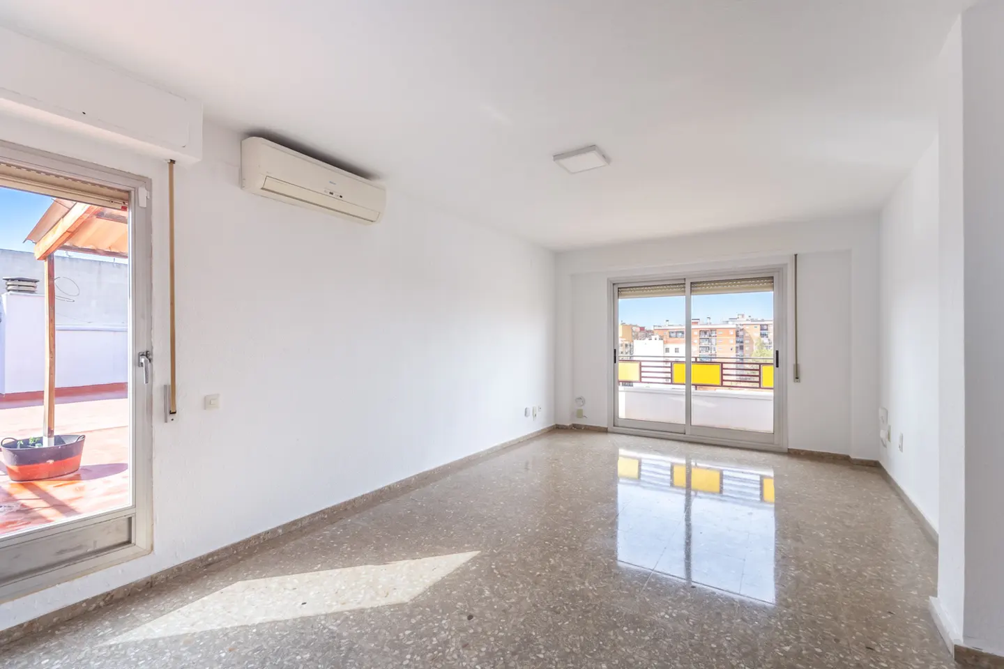Bright, empty room with white walls, speckled tile floors, an air conditioner, and sliding doors leading to a balcony.