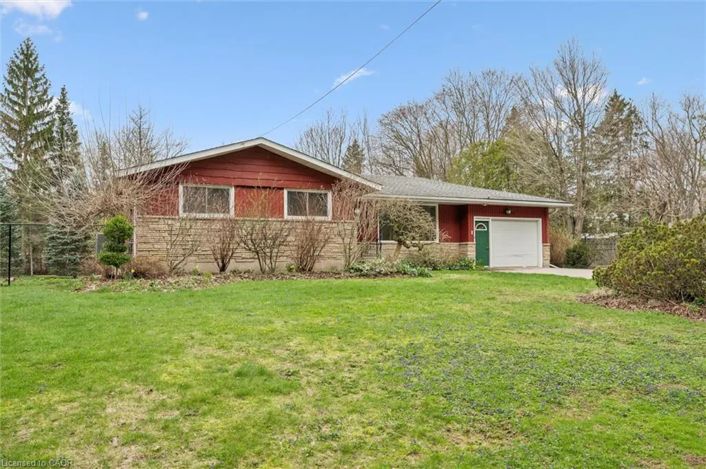A single-story house with red siding and a stone facade, a green door, and a white garage door. A green lawn is in front.