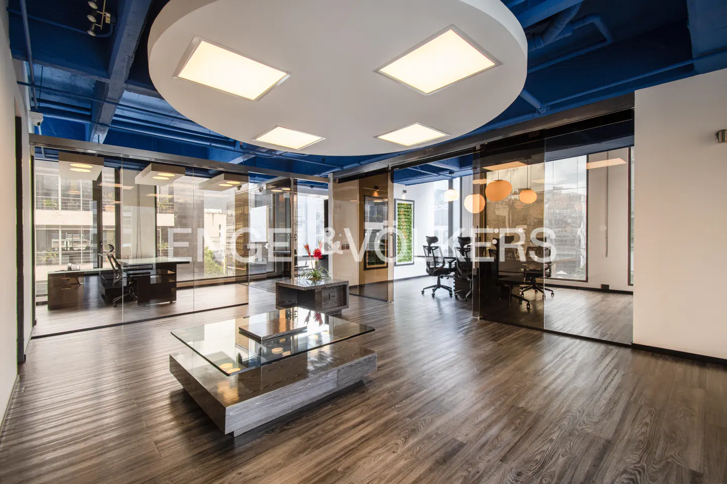 Engel & Völkers office interior with glass walls, wood floors, and modern lighting. Desks and chairs are visible in the background.