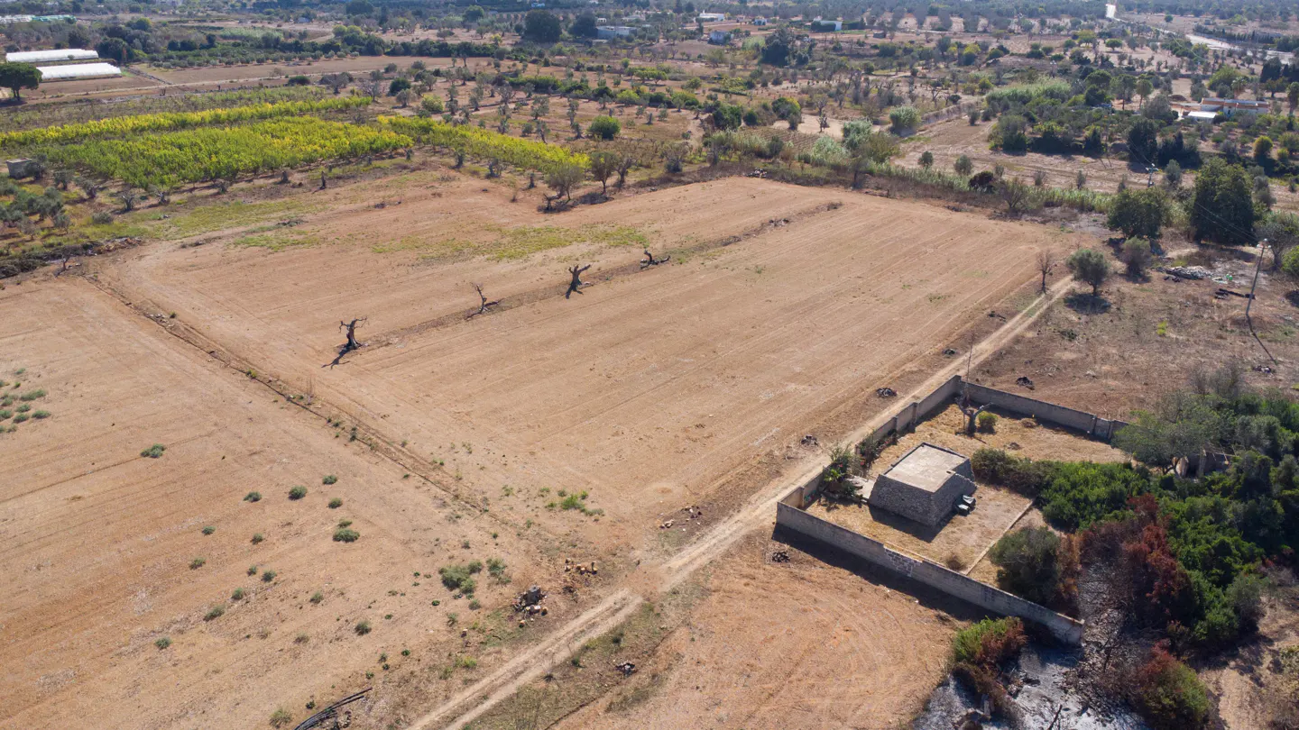 Aerial view of a rural property with a stone house, fields, and trees under a clear blue sky.