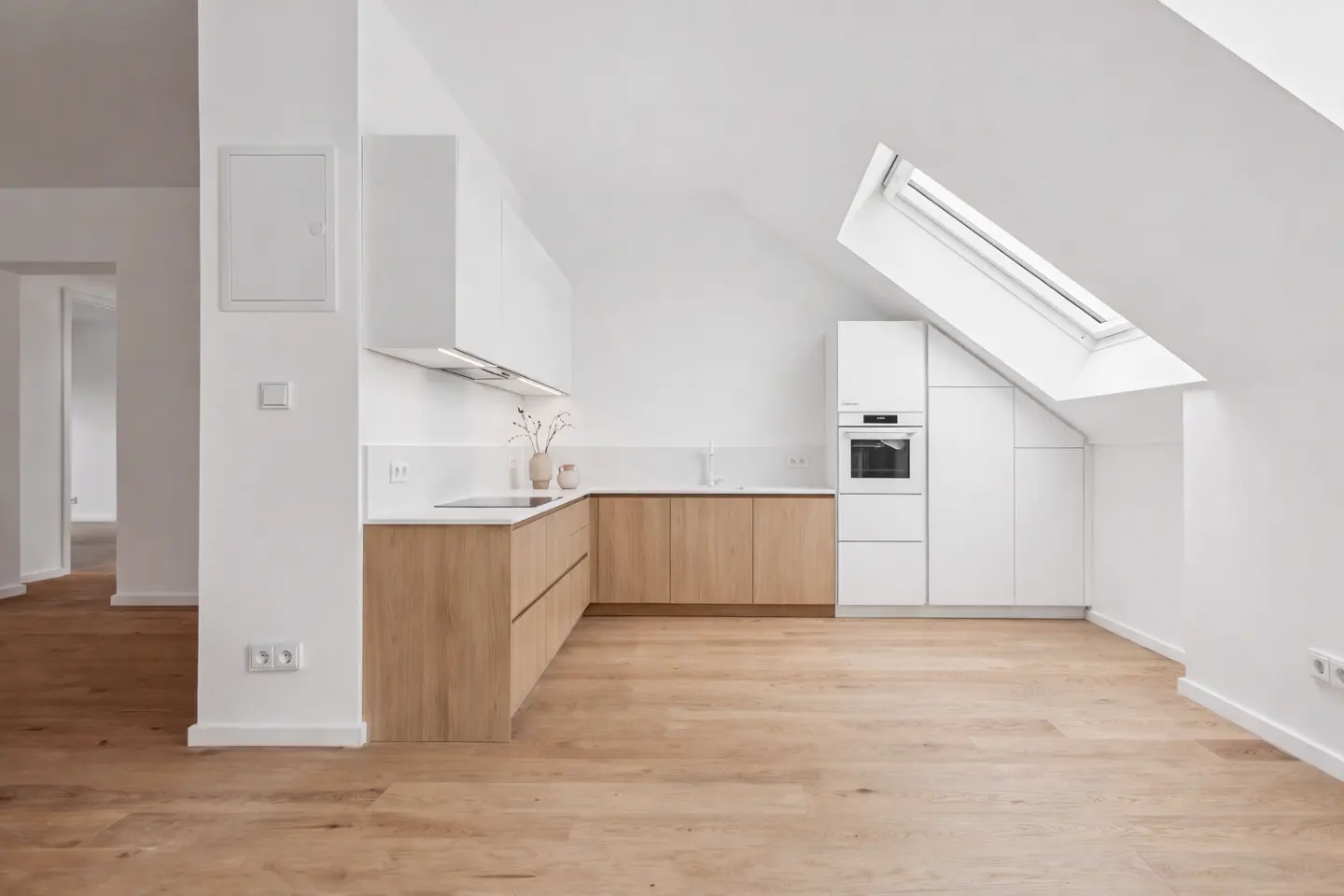 Bright, modern kitchen with white walls, light wood floors, and a skylight. Cabinets are white and light wood.