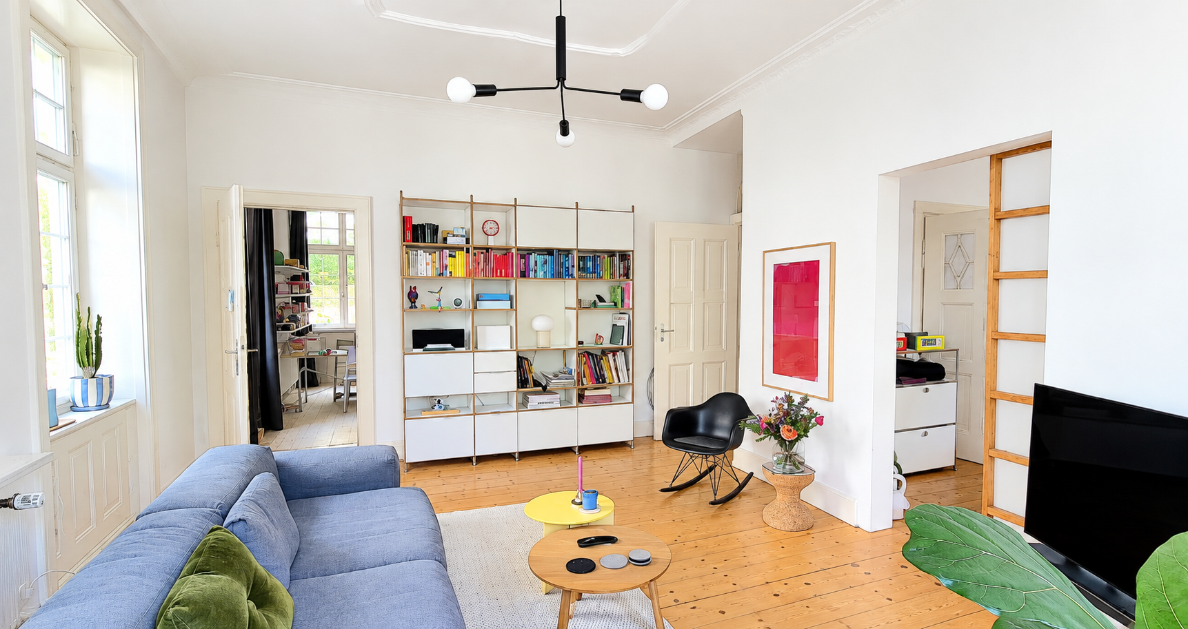 Bright living room with a blue sofa, wooden floors, a modern shelving unit, a black rocking chair, and a TV. [AI-generated text]