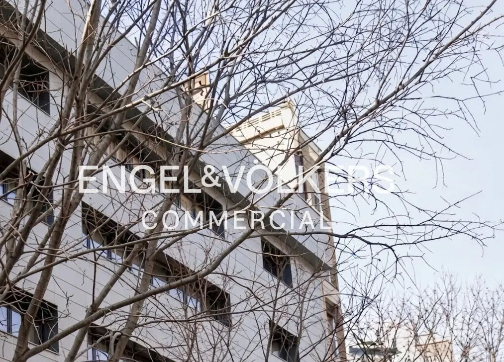 Engel & Volkers Commercial logo on a light gray building with bare trees against a pale blue sky.