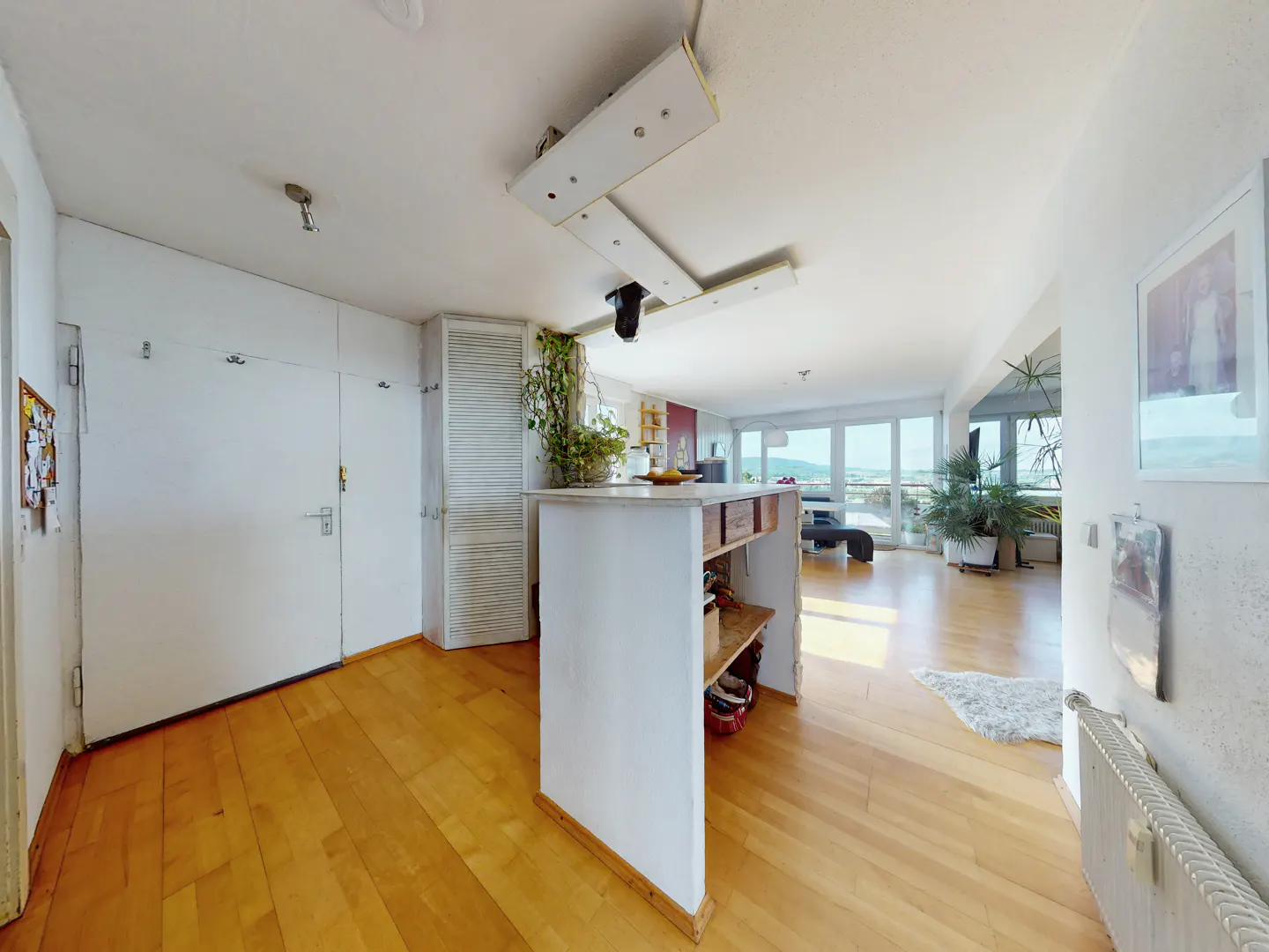 Bright living space with light wood floors, a central white kitchen island, and large windows overlooking a distant view.