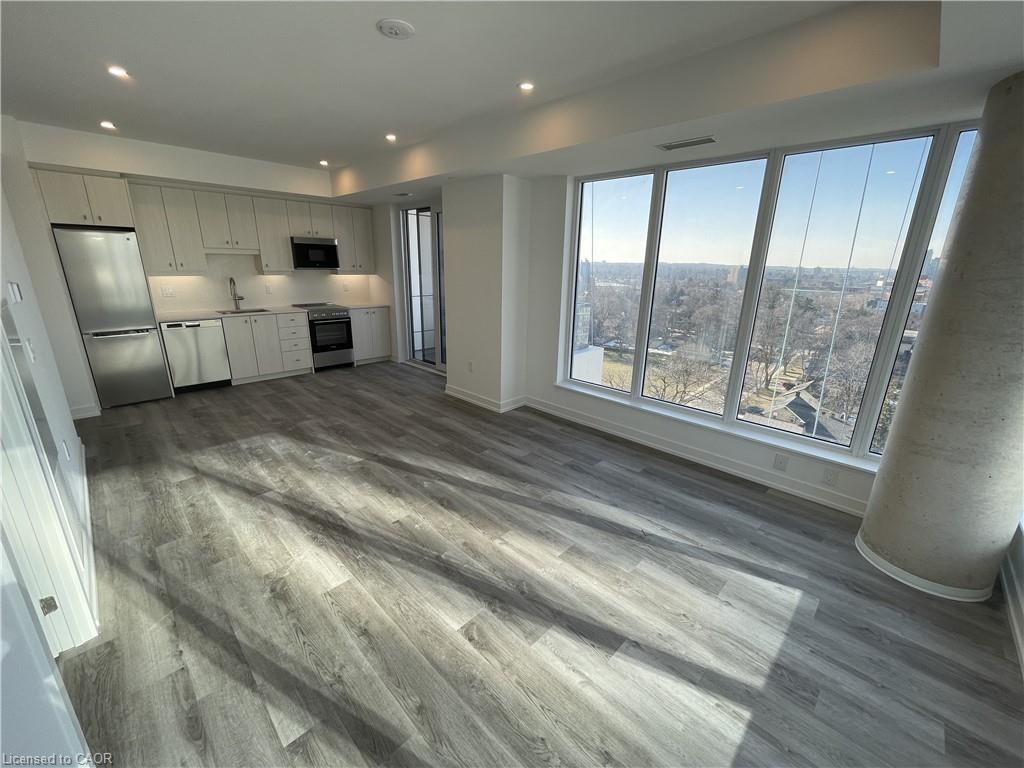 Bright, modern condo interior with gray wood floors, white cabinets, stainless steel appliances, and a large window overlooking a city view.