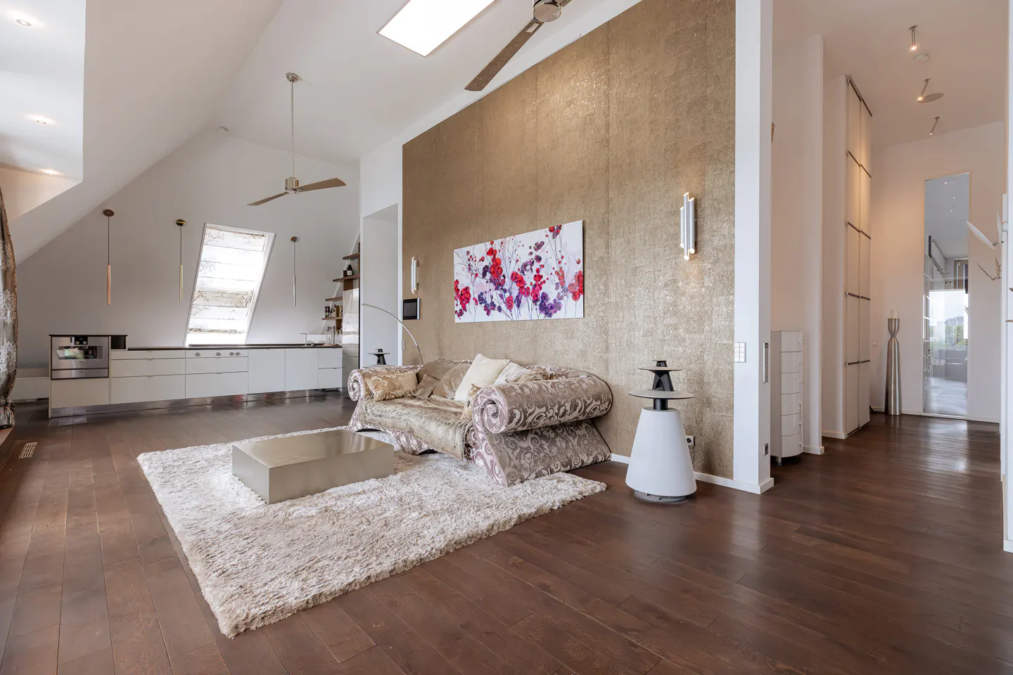 Open-concept living room with hardwood floors, a patterned sofa, and a white shag rug. A gold accent wall features floral art.