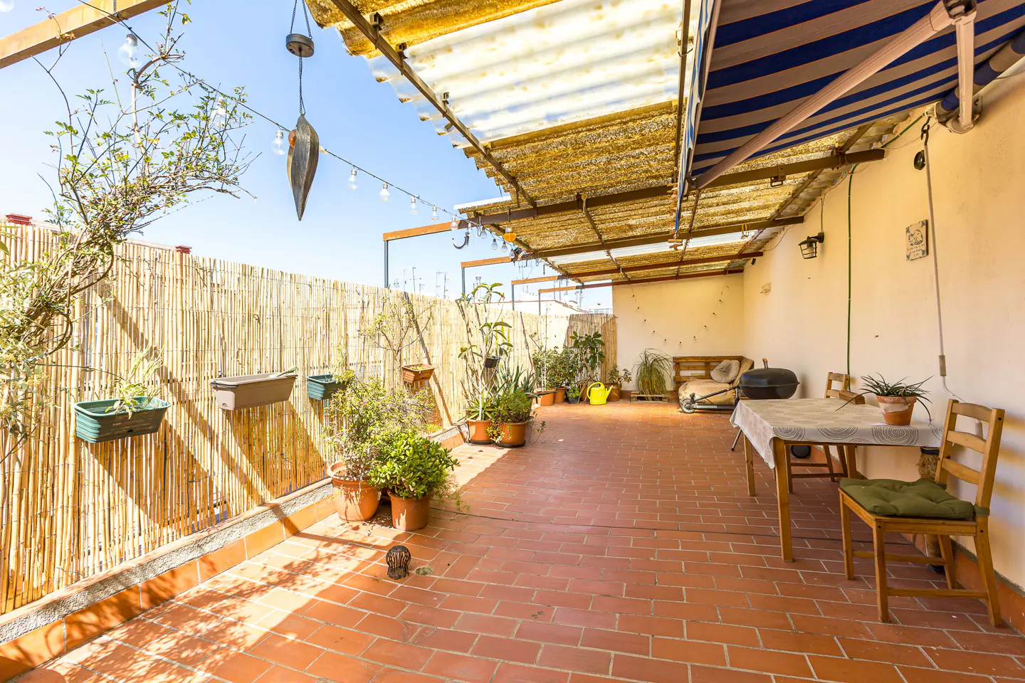 Outdoor patio with brick flooring, bamboo fence, and plants. Table and chairs are set up for dining. String lights hang overhead.