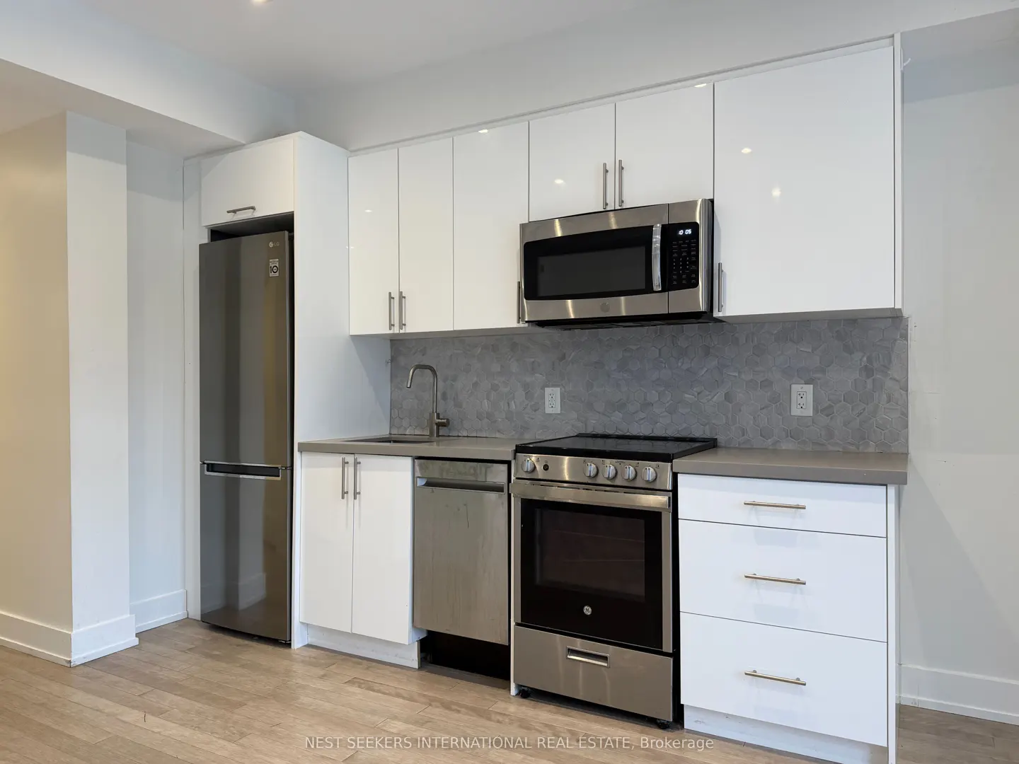 Modern kitchen with white cabinets, stainless steel appliances, and gray backsplash. Light wood floors.