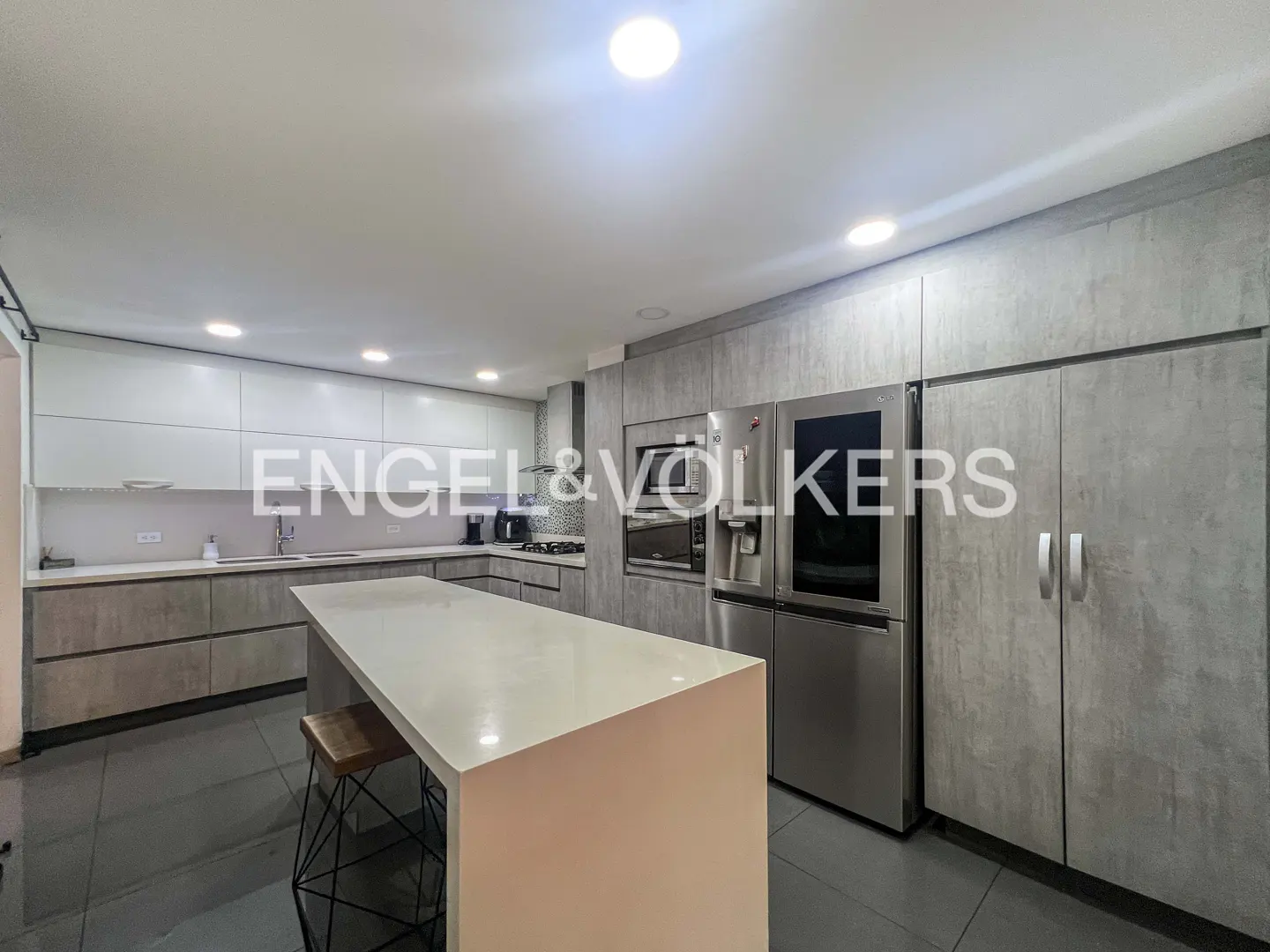 A modern kitchen with gray cabinets, stainless steel appliances, and a white island with a stool.