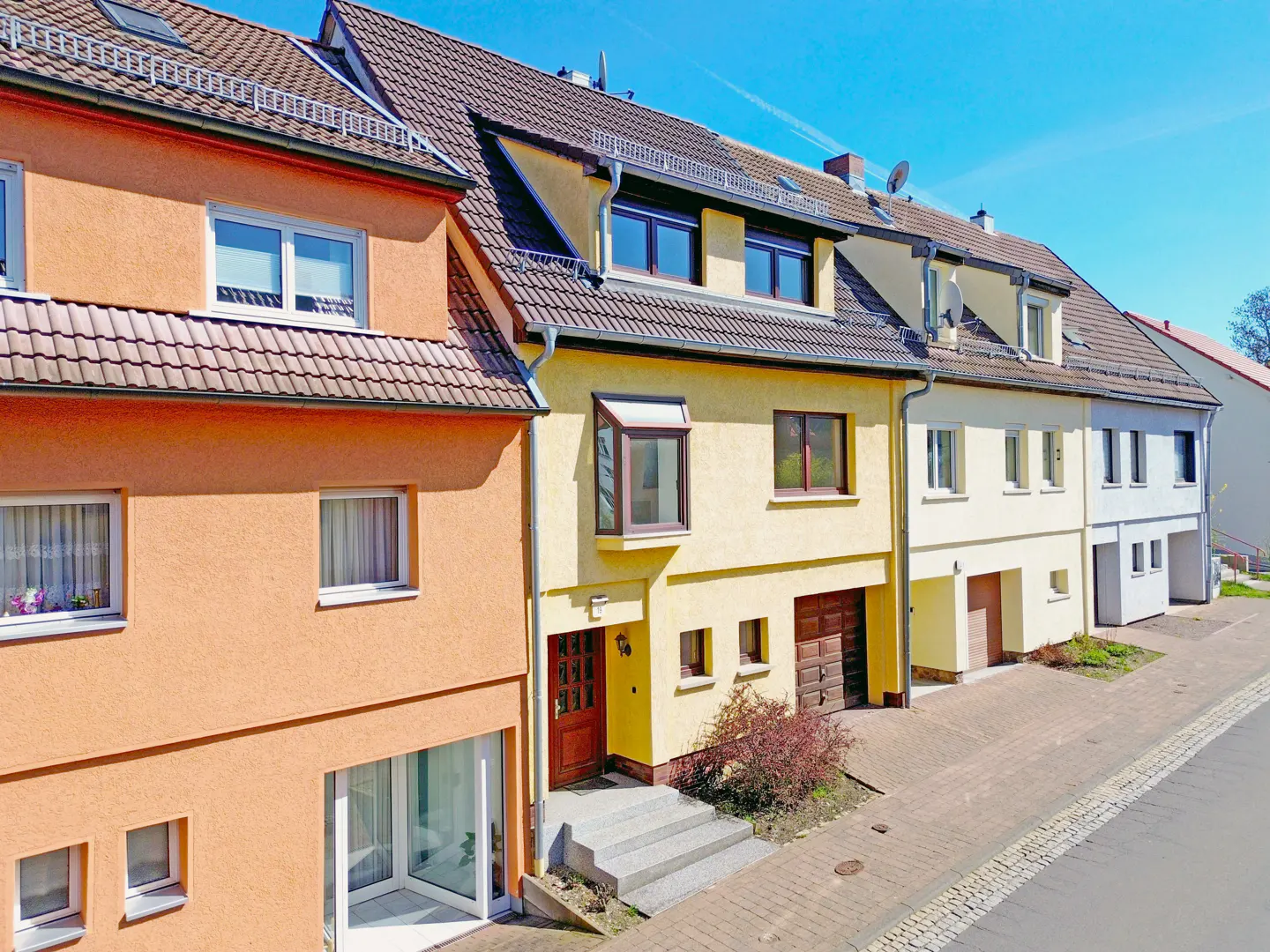 Row of colorful townhouses with orange, yellow, and white facades, brown tiled roofs, and blue sky.