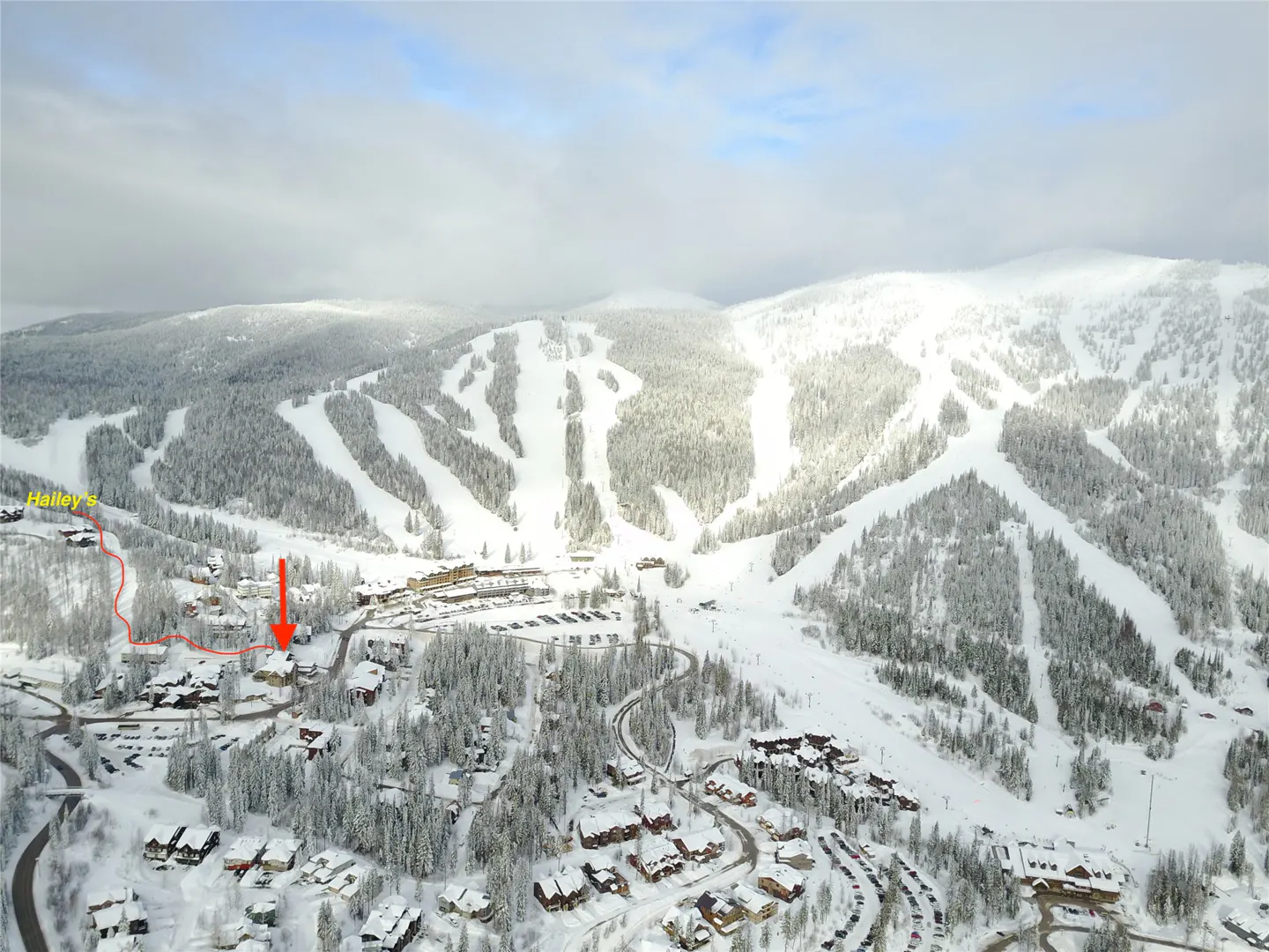 Aerial view of a snow-covered mountain with ski runs, houses, and trees. A red arrow points to a house, and a red line indicates a path to "Hailey's."