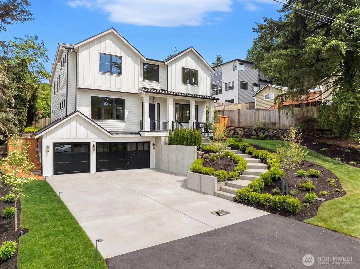 Two-story white farmhouse with black trim and a two-car garage. Landscaped front yard with concrete steps leading to the front door.