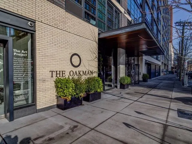 Exterior view of The Oakman building with brick facade, planters, and glass windows.