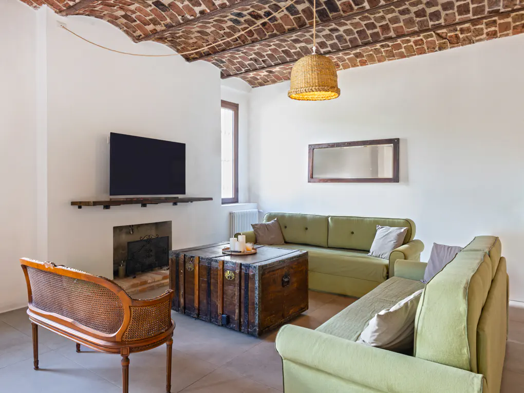 Living room with brick ceiling, light green sofas, and a wooden trunk as a coffee table. A TV is mounted above a fireplace.