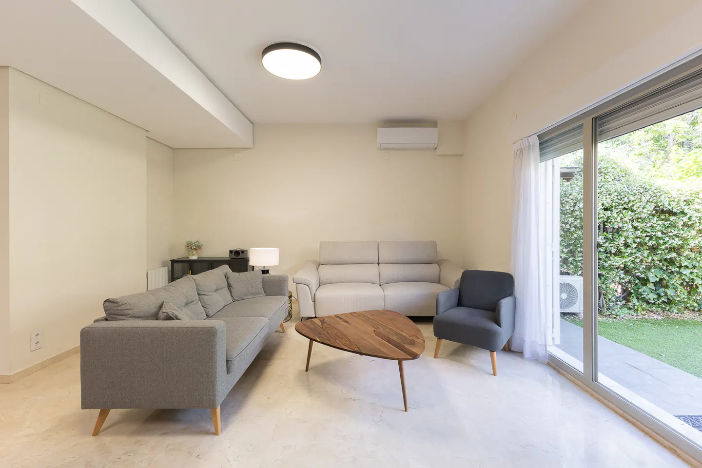 Modern living room with a grey sofa, a light grey loveseat, a dark grey armchair, and a wooden triangular coffee table.