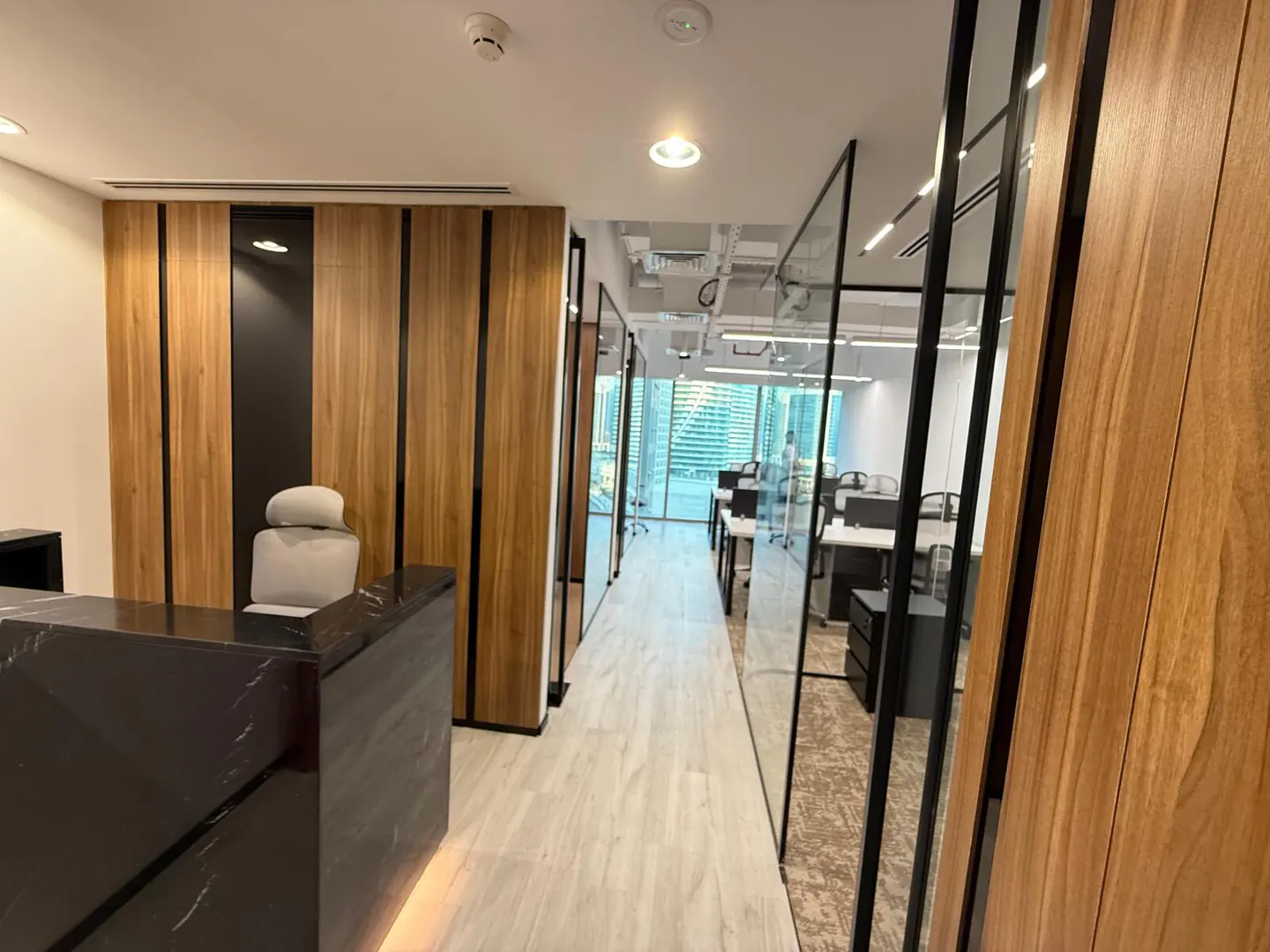 Office interior with a black marble reception desk, wood paneled walls, and glass-walled offices with desks and chairs.