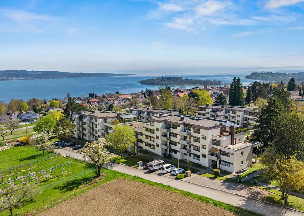 Aerial view of modern apartment buildings with lake and mountains in the background on a sunny day.