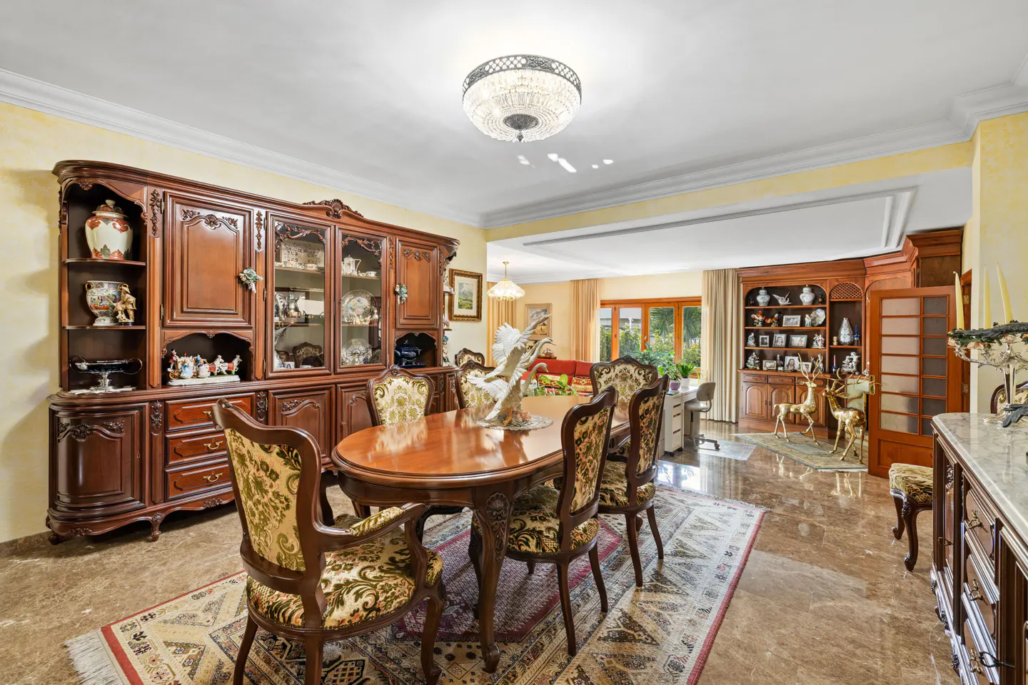 A formal dining room with a large wooden table, upholstered chairs, and a crystal chandelier.