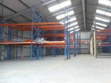 A warehouse interior with blue metal shelving and orange support beams. Skylights illuminate the space.