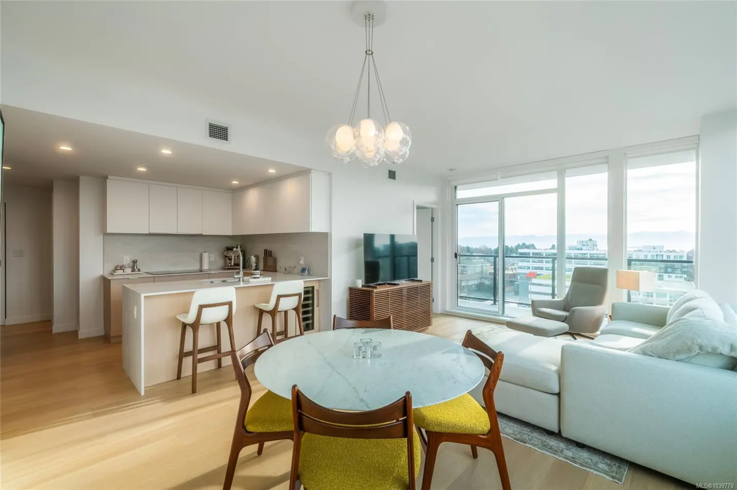Modern open-concept living area with a white kitchen, marble dining table, yellow chairs, and a light blue sectional sofa.