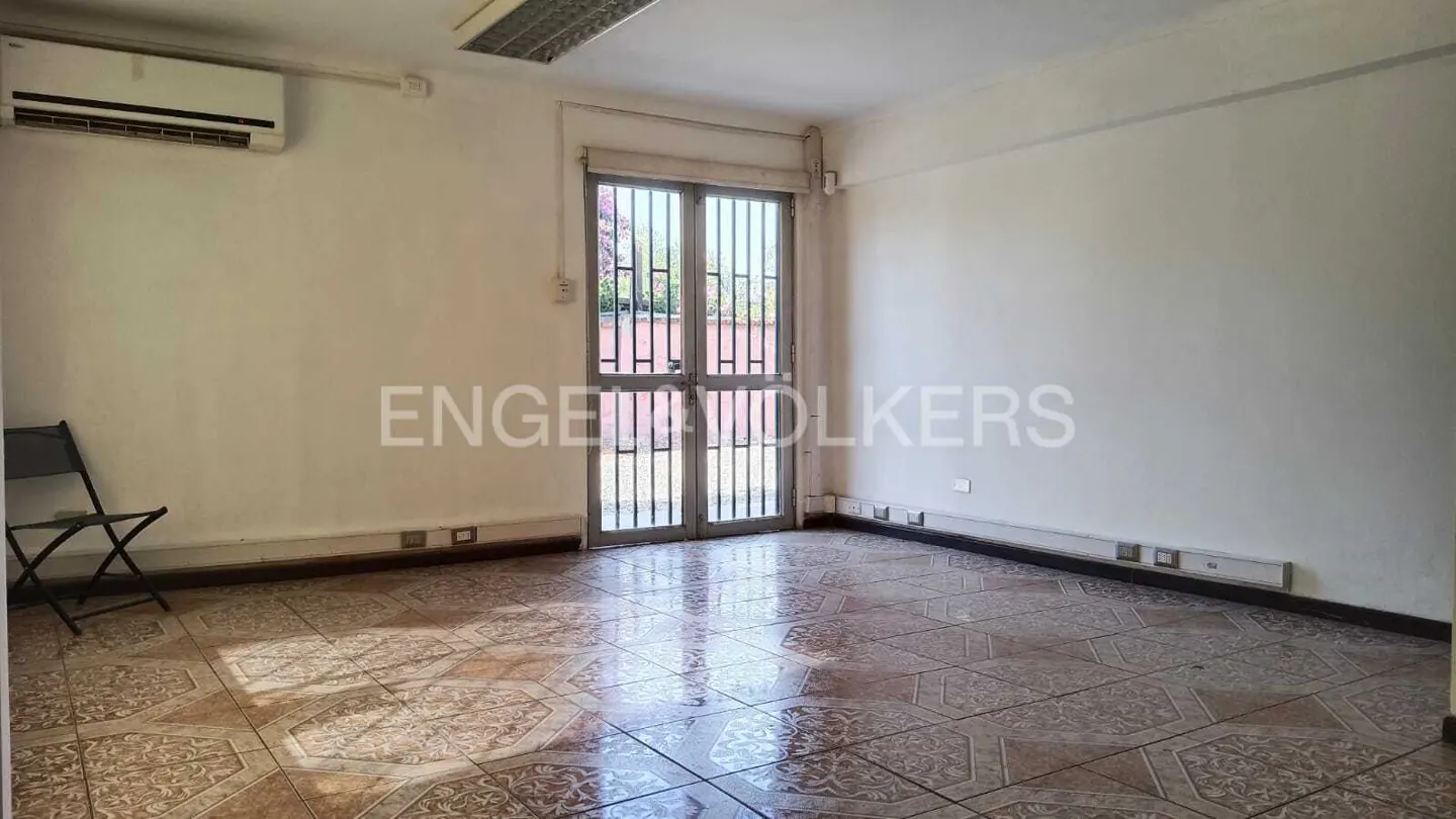 Empty room with tiled floor, white walls, and metal-barred double doors leading to a balcony. A/C unit on the wall.