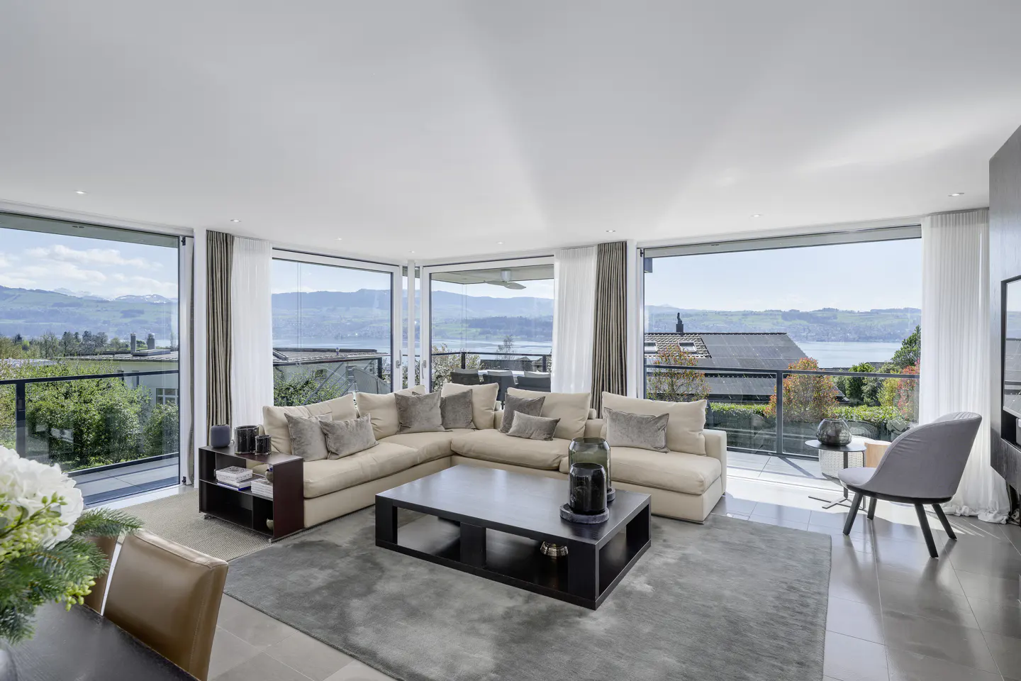 Bright living room with beige sectional sofa, dark wood coffee table, and floor-to-ceiling windows with lake view.