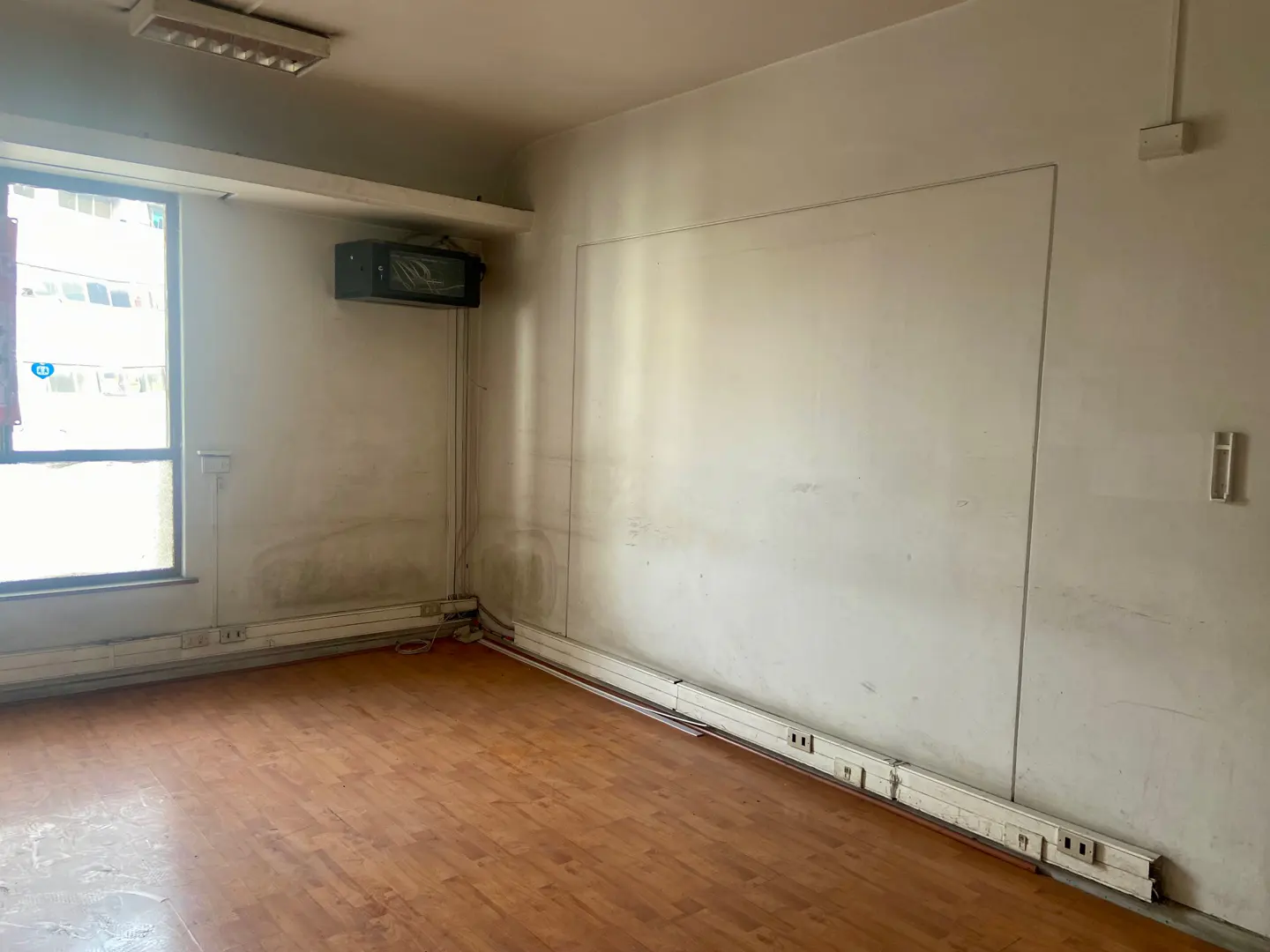 Empty room with wood floors, white walls, and a window. There is an air conditioning unit on the wall and baseboard heaters along the floor.