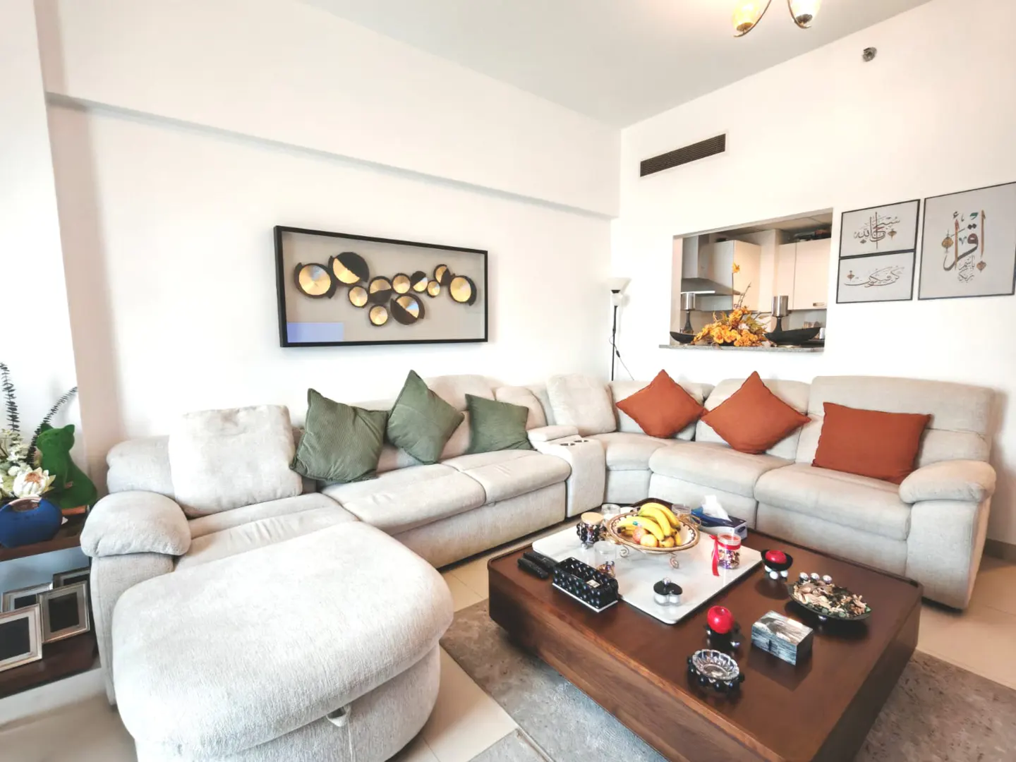 Bright living room with a large, light beige sectional sofa, brown coffee table, and modern art on the white walls.