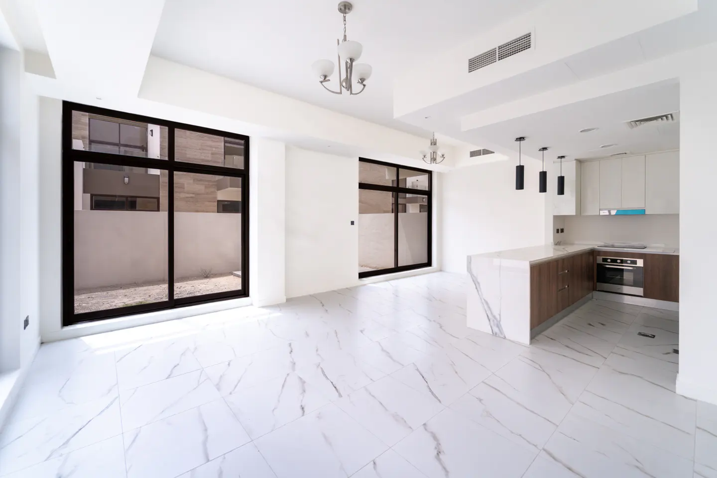 Bright, modern open-plan living space with white marble floors, black-framed windows, and a kitchen with a marble island.