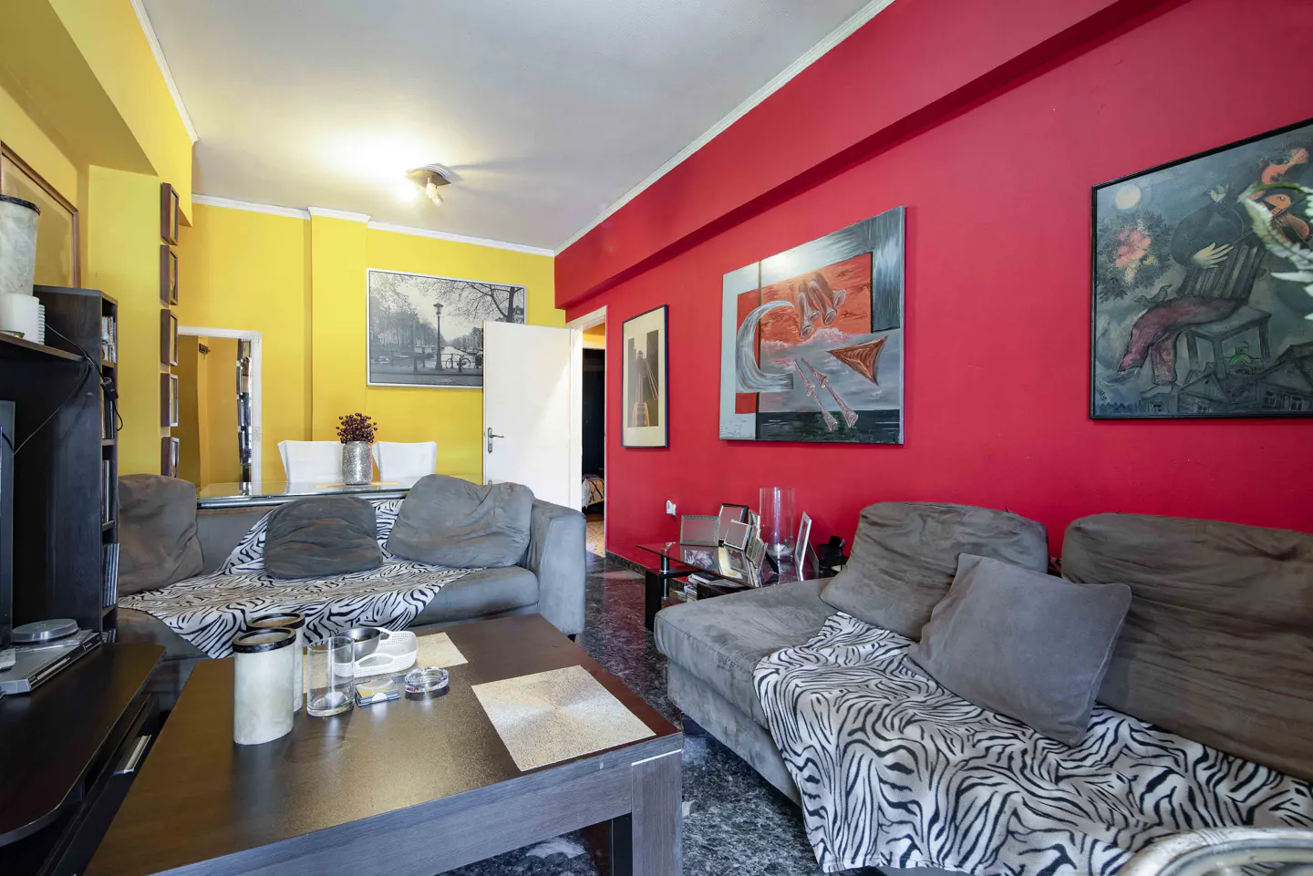 Living room with grey sofas, zebra-print throws, a dark coffee table, and walls painted in vibrant red and yellow.