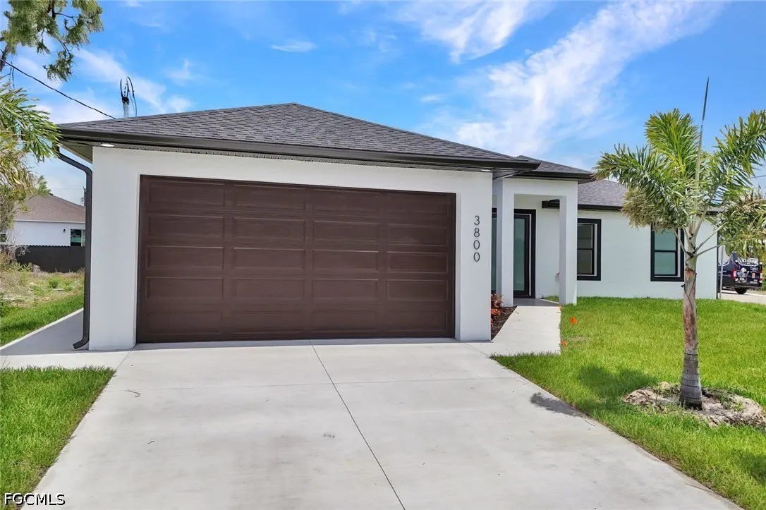 A modern, one-story white house with a brown garage door and a concrete driveway under a blue sky.