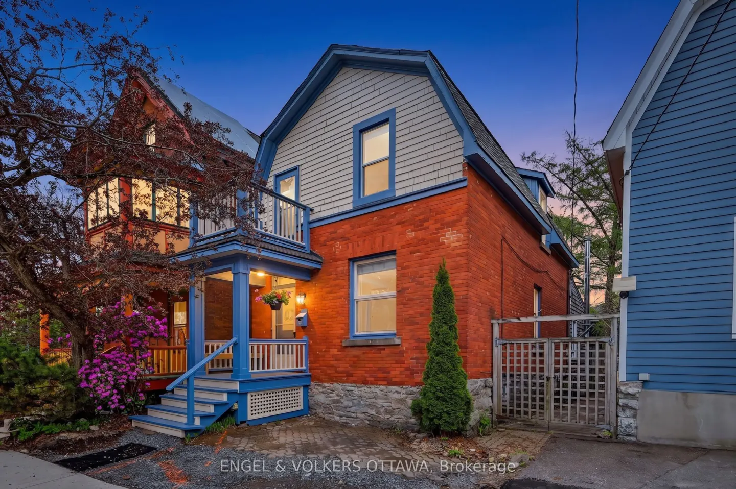 Exterior view of a two-story red brick house with blue trim and a small porch at dusk.