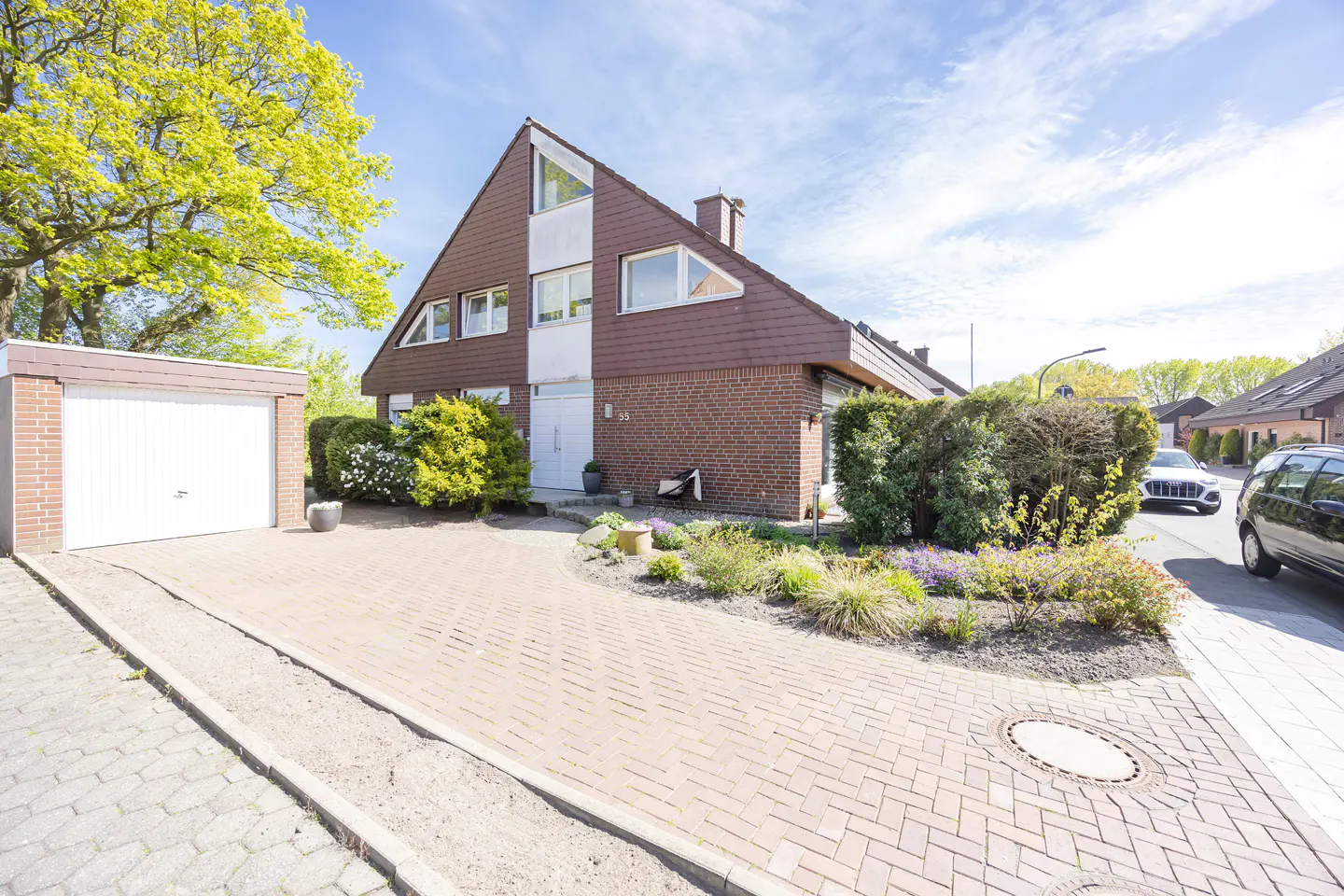 A brown brick house with a garage and a brick driveway on a sunny day.