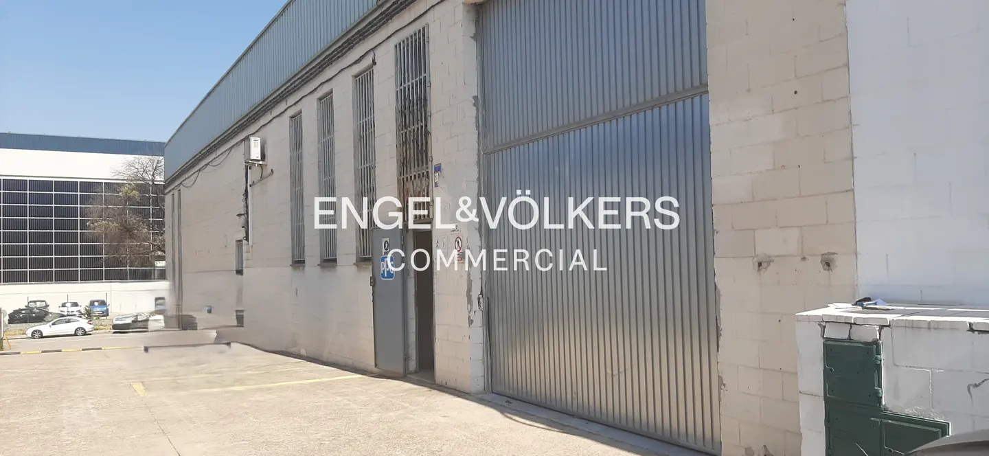 Exterior view of a commercial warehouse with a large metal sliding door, white block walls, and a paved parking area.