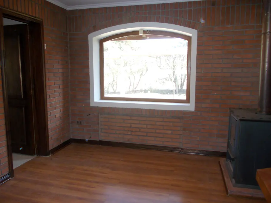 Brick-walled room with wood floors, a white-framed window showing trees, and a black wood-burning stove.