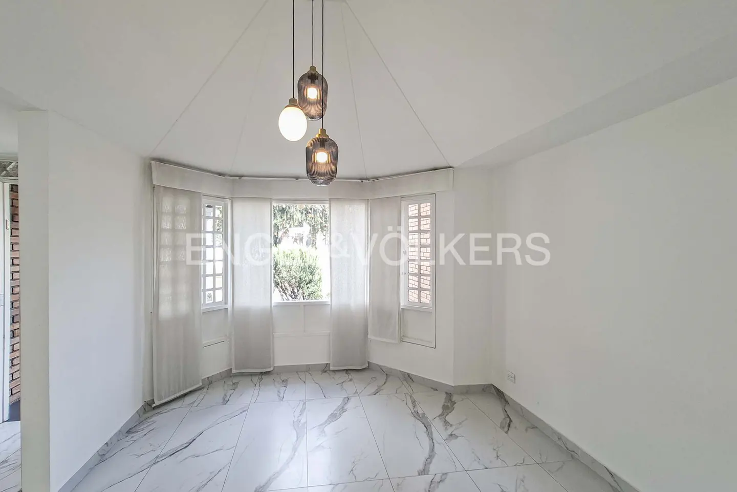 Empty room with white walls, marble-patterned tile floors, a bay window with sheer curtains, and three hanging pendant lights.