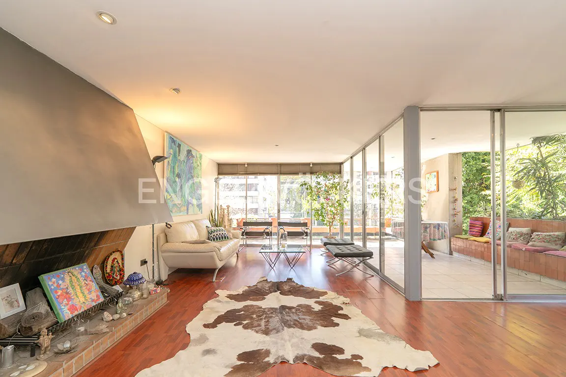 Bright living room with a fireplace, white sofa, and a cowhide rug on a wooden floor. Sliding glass doors lead to a balcony with plants.
