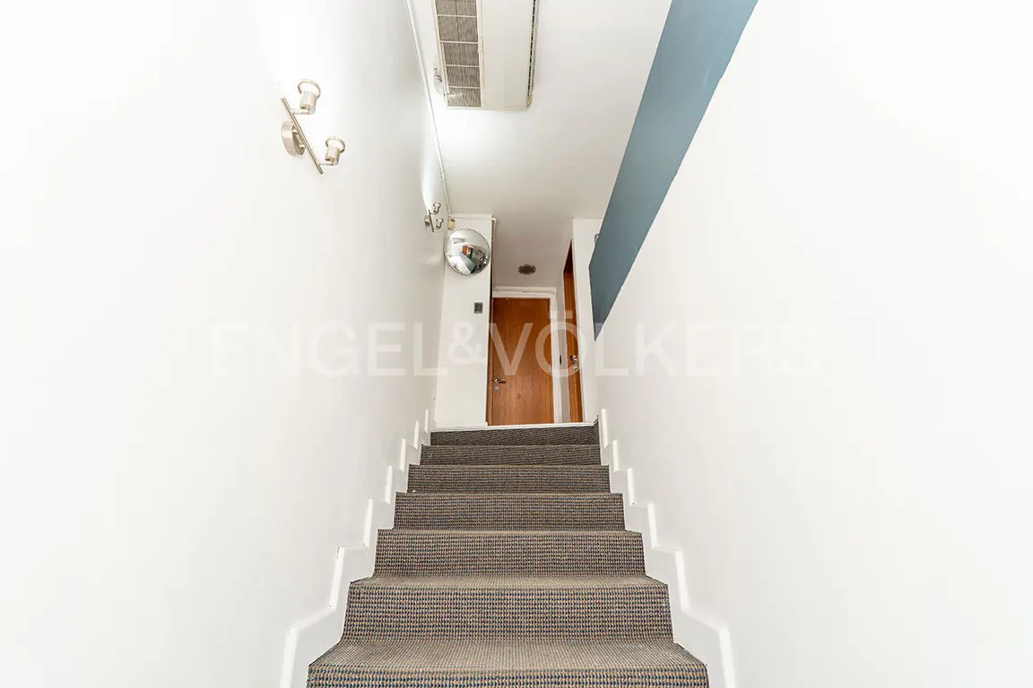 A view up a carpeted staircase with white walls, leading to a wooden door. A silver coat rack is on the left wall.