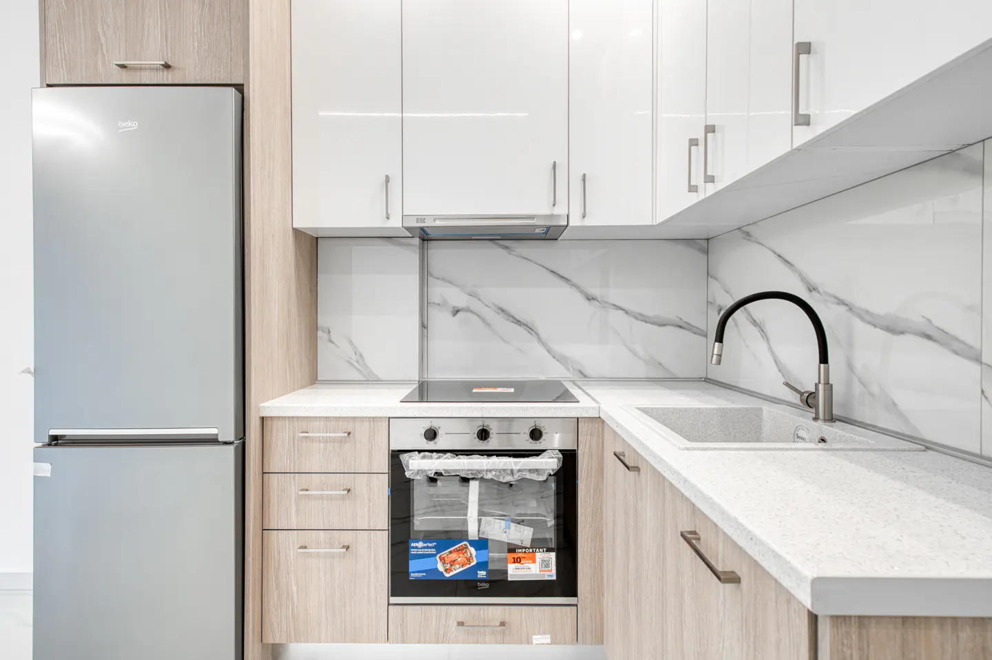A modern kitchen with white cabinets, marble backsplash, stainless steel appliances, and light wood-tone lower cabinets.