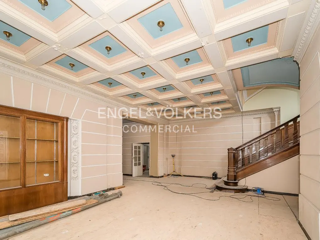 A spacious room with a decorative ceiling, wooden staircase, and the Engel & Völkers Commercial logo.