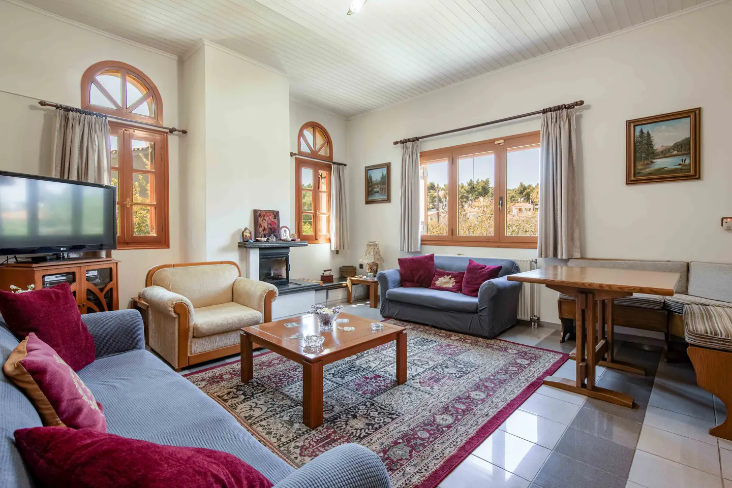 Living room with blue sofas, beige armchair, wood table, fireplace, and patterned rug. Natural light from arched windows.