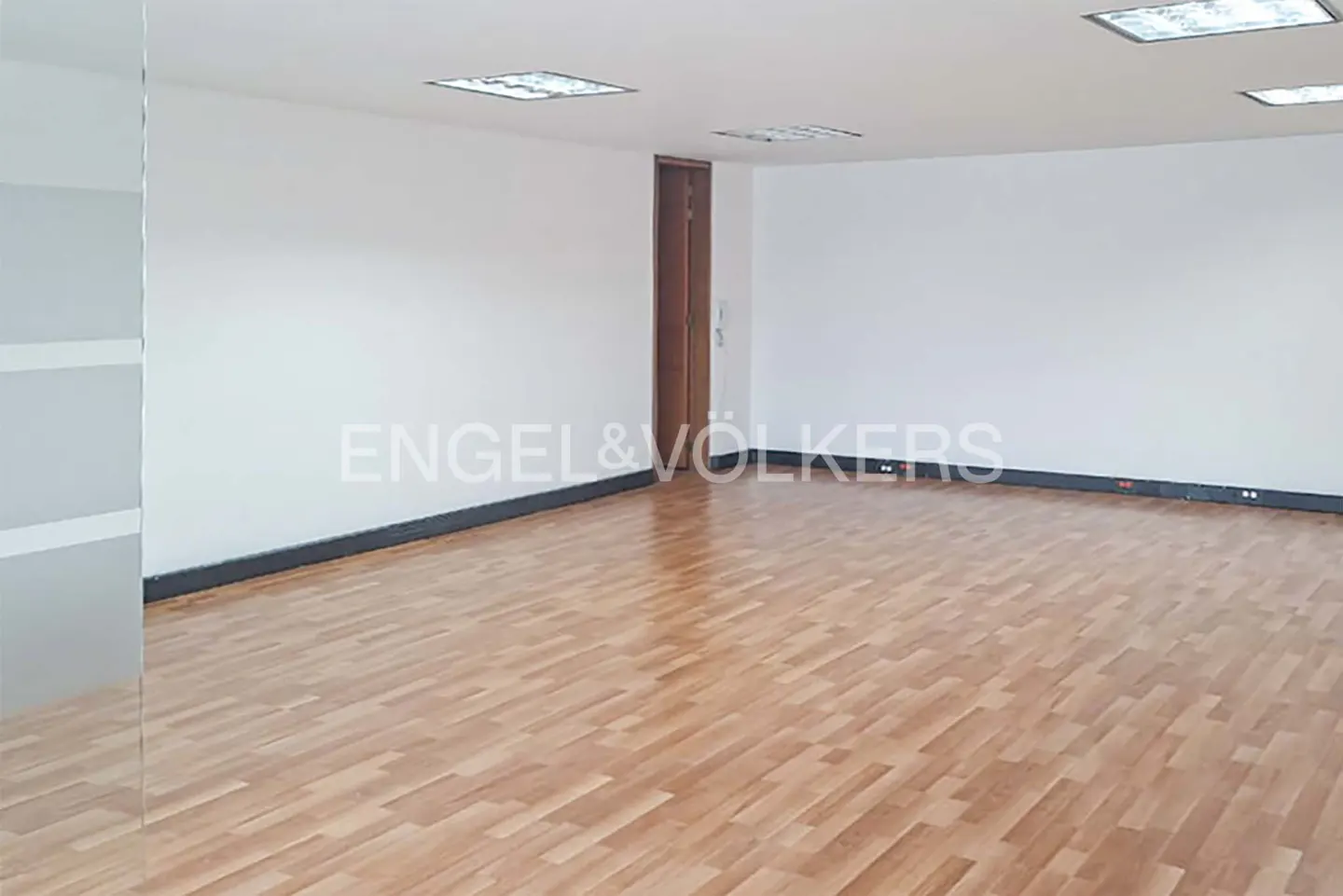 Empty office space with wood floors, white walls, and a brown door. Engel & Völkers logo is visible.