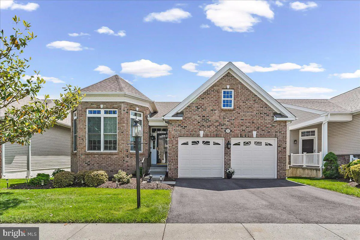 A brick house with a two-car garage, green lawn, and blue sky with white clouds.