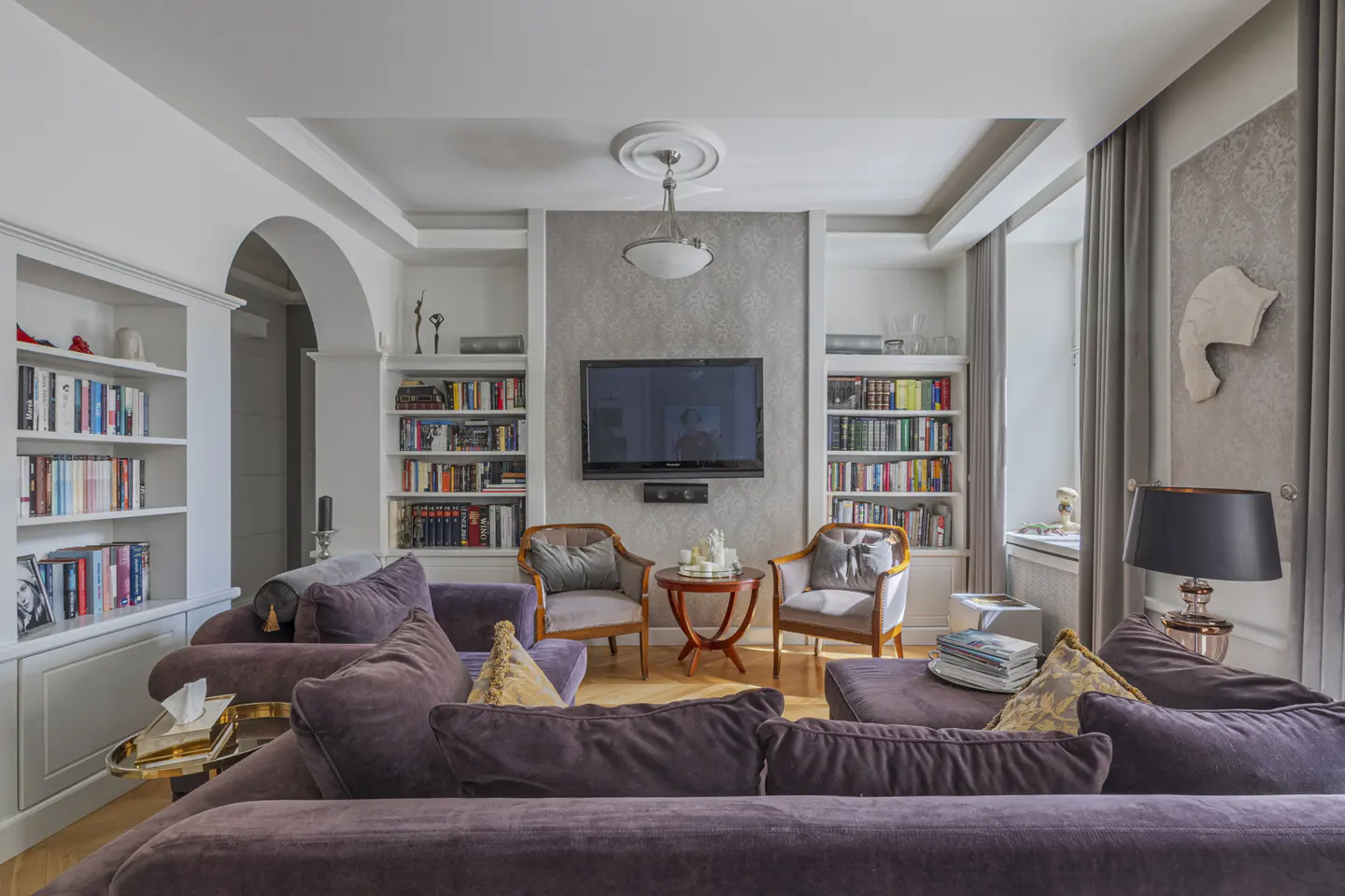 Living room with a purple sofa, two chairs, a TV, and bookshelves filled with books.