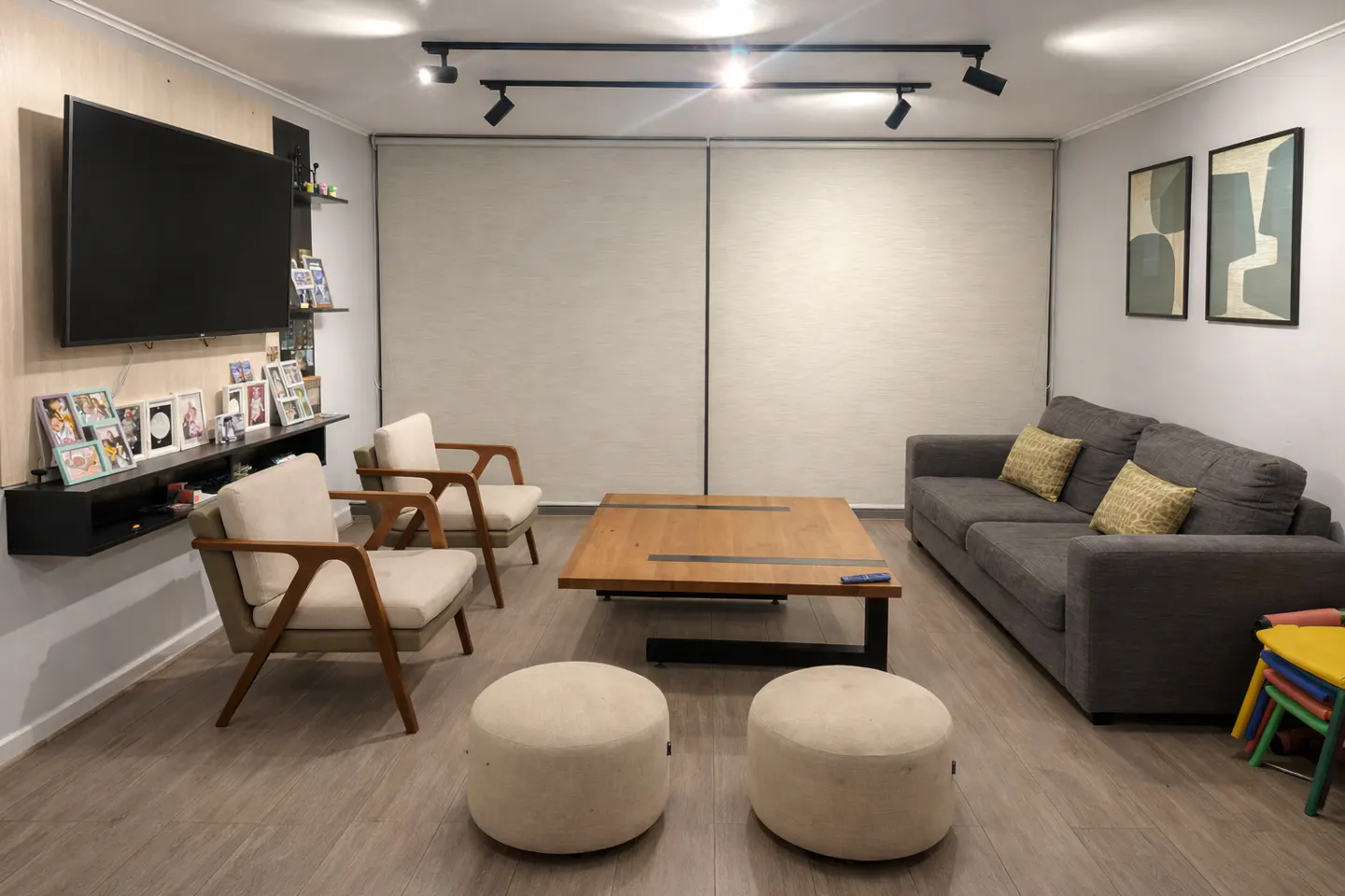 Living room with gray sofa, two cream armchairs, wood coffee table, and TV. Two cream ottomans sit in the foreground.