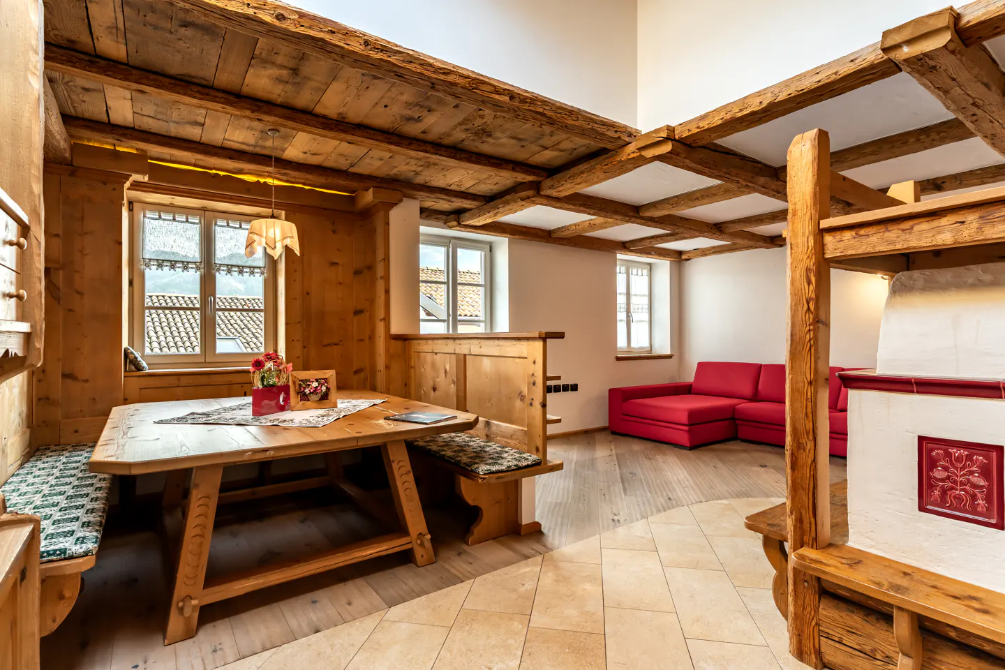 Rustic dining area with wooden table and benches, exposed ceiling beams, and a bright red sofa in the background.