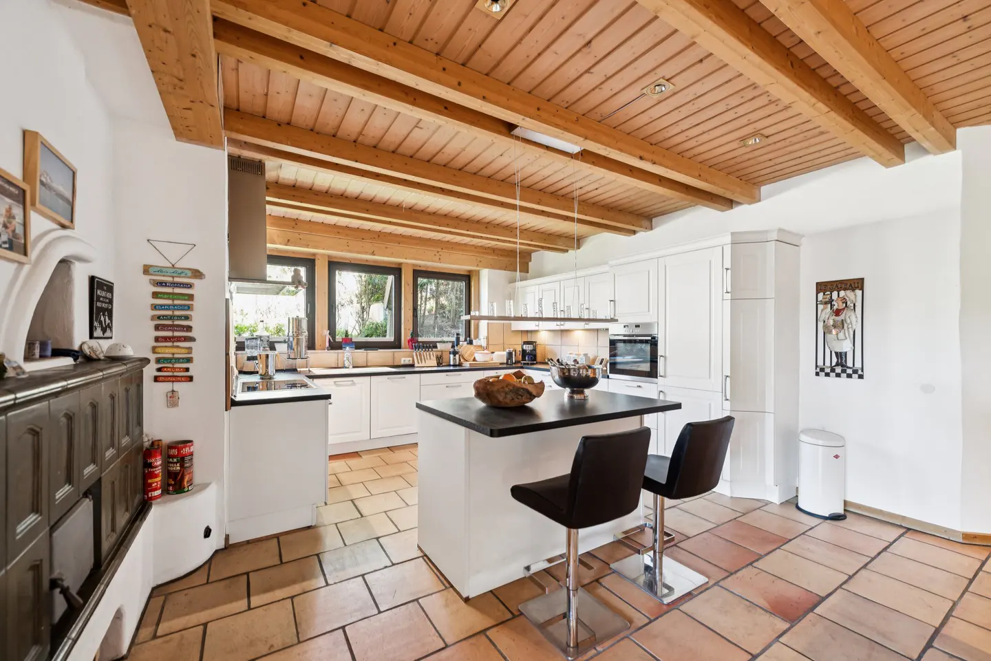 A bright kitchen with white cabinets, a black countertop island with two stools, and a wood-beamed ceiling.