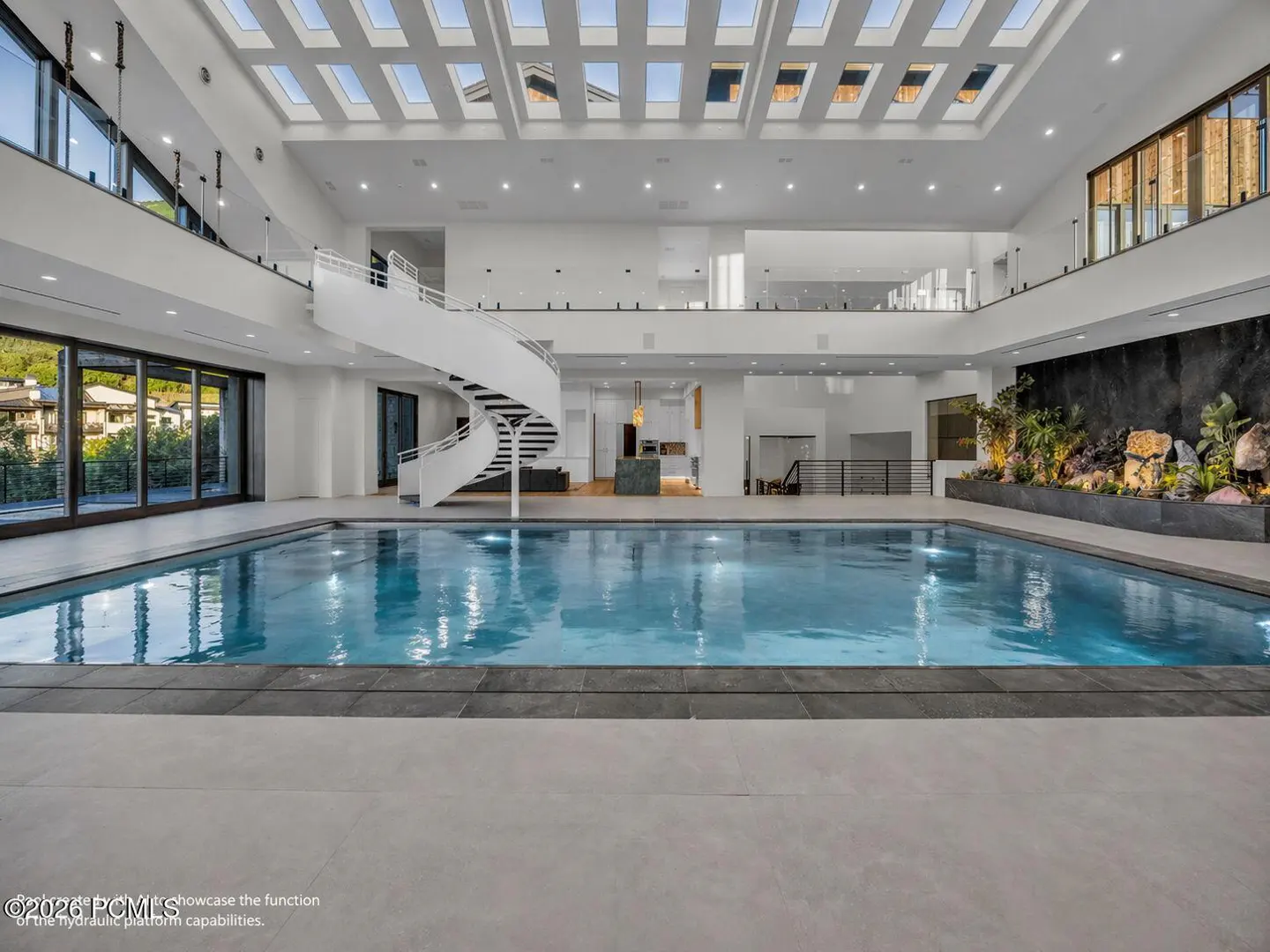 Indoor pool with a white spiral staircase, skylights, and a rock garden. The pool is blue and the room is white.