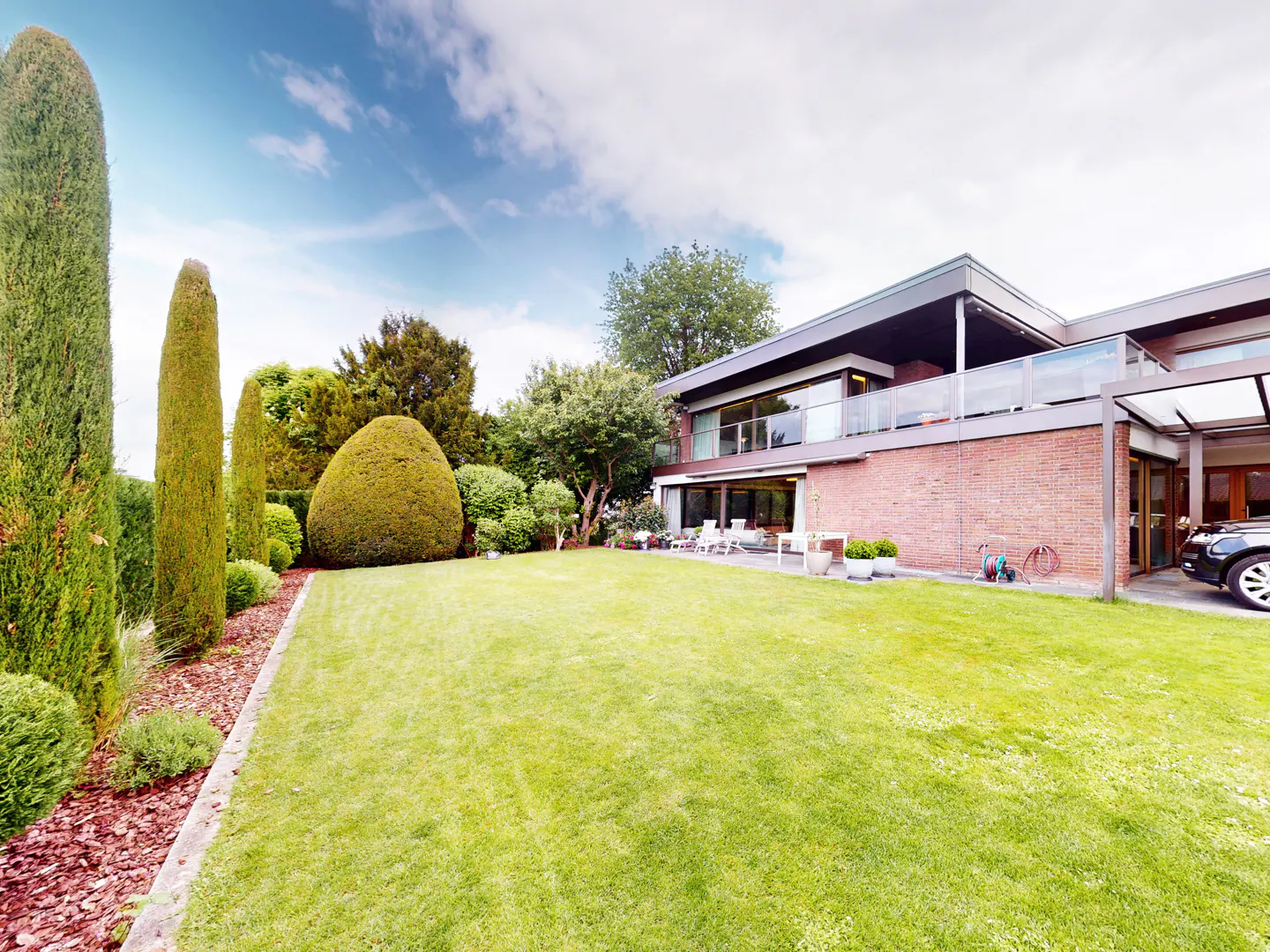 A wide shot of a large green lawn, trees, and a two-story brick house under a blue sky.