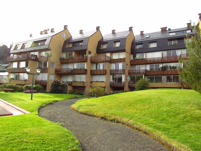 Three-story apartment building with brown balconies and a gray gravel path through a green lawn.